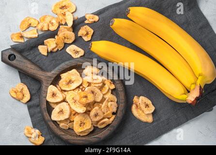 Banana chips e banane fresche su sfondo grigio. Vista dall'alto. Dolci sani naturali. Foto Stock