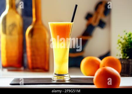 Succo d'arancia appena spremuto su un supporto nero e tre arance accanto ad esso Foto Stock