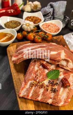 Costolette di maiale crude con spezie. Carne cruda sulla tavola della cucina. Preparazione di marinata di miele e peperoncini. Barbecue estivo. Foto Stock