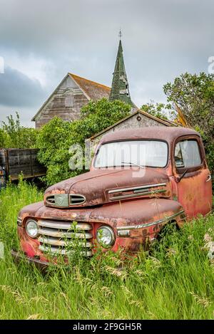 Weyburn, SK- 19 luglio 2020: Classico camion del raccoglitore rosso Mercury serie M abbandonato con la chiesa presbiteriana di Froude sullo sfondo Foto Stock