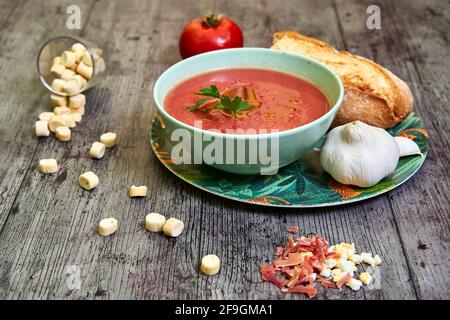 Ciotola andalusa di gazpacho con EVOO e prezzemolo a fuoco, accompagnata da pane e aglio. Crostini fuori fuoco, prosciutto di Serrano, uovo e un pomodoro. Conce Foto Stock