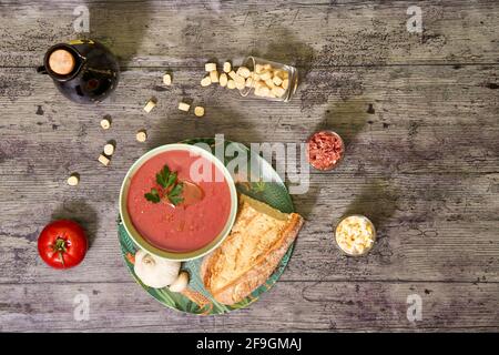 Vista Zenith della ciotola andalusa di gazpacho con pane e aglio. Intorno ci sono crostini, prosciutto di Serrano e uovo sminuzzato bollito. EVOO, e un pomodoro. Conc Foto Stock