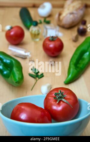 Fuoco selettivo degli ingredienti andalusi del gazpacho che lasciano la ciotola e si sparge attraverso il tavolo. Solo pomodori a fuoco, altre verdure fuori da fo Foto Stock