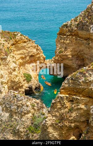 Tre kayak nel mare turchese navigando attraverso archi di roccia, scogliere di rocce di arenaria, Algarve, Lagos, Portogallo Foto Stock