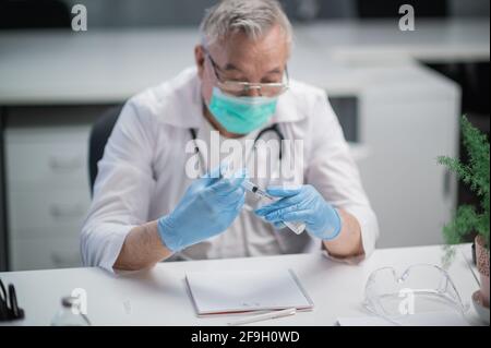 Un medico dell'ufficio medico vaccina la popolazione contro il ceppo di covid - 19 virus. Riempie la siringa con il medicinale per iniezione. Foto Stock