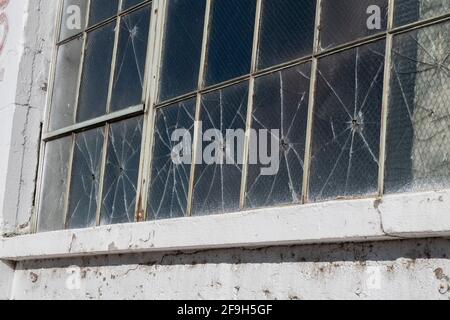 Una fila di finestre in un edificio abbandonato sembra essere stata sparata con un pellet o pistola bb. Foto Stock