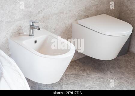 bide e toilette bianche, su piastrelle in ceramica grigia in bagno Foto Stock