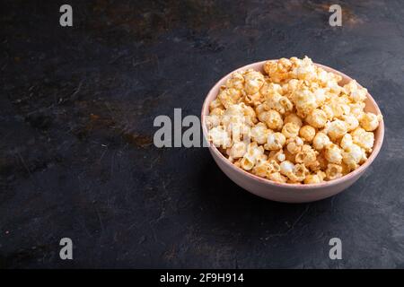 Popcorn con caramello in ceramica su fondo nero di cemento. Vista laterale, spazio di copia. Foto Stock