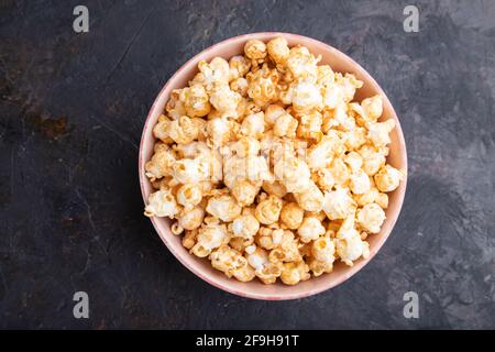 Popcorn con caramello in ceramica su fondo nero di cemento. Vista dall'alto, disposizione piatta, primo piano. Foto Stock