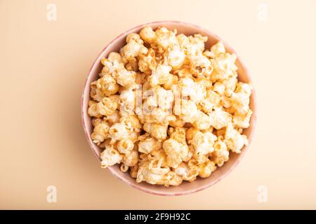 Popcorn con caramello in ceramica su sfondo arancione pastello. Vista dall'alto, disposizione piatta, primo piano. Foto Stock