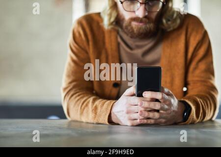 Minimo ritaglio di uomo bearded utilizzando il telefono cellulare con messa a fuoco sulle mani maschili tenendo smartphone, spazio di copia Foto Stock
