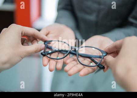 la mano di un assistente di negozio dà un paio di occhiali a. la mano di un cliente Foto Stock