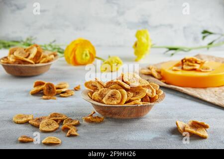 Banana chips cibo sano, frutta secca e patatine vegetali sane, sano spuntino vegano su sfondo di fiori gialli Foto Stock