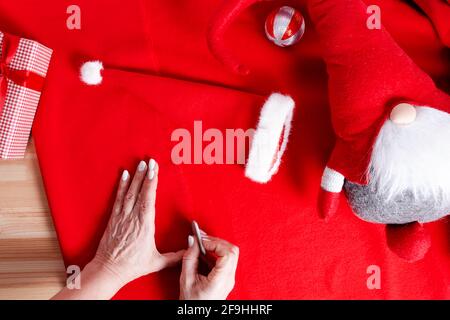 Nonna cucire piccolo cappello di Santa per i nipoti. Primo piano. Gesso del sarto nelle mani per fare il modello di cucitura. Preparazione per la Fiera di Natale della scuola. Foto Stock