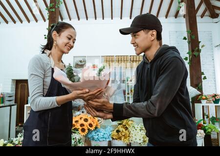 sorridente giovane negoziante che indossa un grembiule. servendo gli acquirenti di fiori di flanella maschio Foto Stock