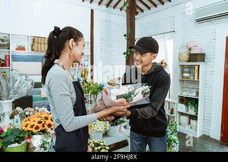 sorridente giovane negoziante che indossa un grembiule. servendo gli acquirenti di fiori di flanella maschio Foto Stock