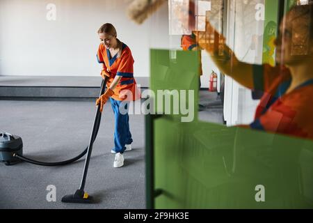 Janitor che aspira il tappeto alla presenza dei suoi colleghi Foto Stock