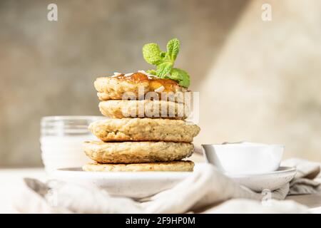 Una pila di frittelle vegetariane di farinata d'avena per colazione decorate con noci, marmellata e menta, sfondo di pietra chiaro. Messa a fuoco selettiva. Foto Stock