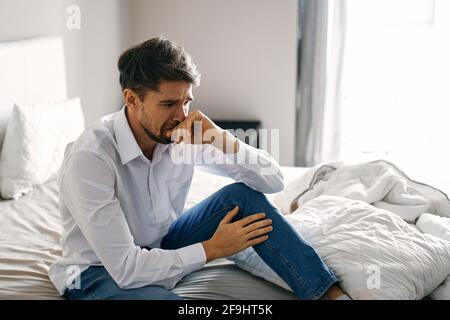 Un uomo solitario si siede su un letto in un luminoso camera vicino a una finestra vista dall'alto Foto Stock