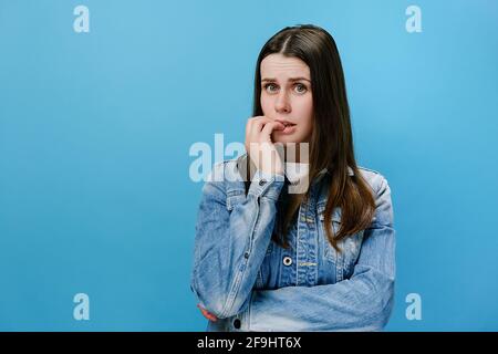 Preoccupata giovane ragazza ripiegata le mani vicino alla bocca, unghie gnawing, giovane donna si sente incerta, stressata. Confuso brunette femmina con paura Foto Stock