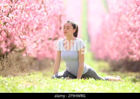 Donna concentrata che pratica l'esercizio di yoga sull'erba in un campo fiorito in primavera Foto Stock