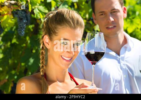 Donna in armonia con un bicchiere di vino in mano e sorridente, uomo in background Foto Stock