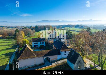 Foto con drone di un villaggio, caratterizzato da terreni agricoli con case circondate da un ambiente lussureggiante e montagne a Faveges, in Francia Foto Stock