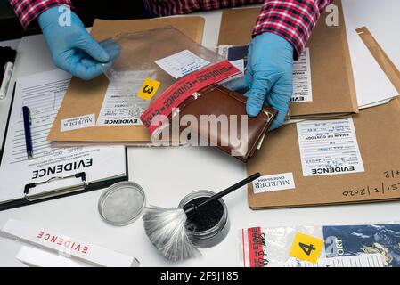 Un ufficiale di polizia specializzato prende il portafoglio con denaro da un sacchetto di prove di omicidio, immagine concettuale Foto Stock