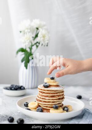 mano per bambini e pila di frittelle con frutti di bosco. deliziosa colazione fatta in casa. immagine verticale Foto Stock