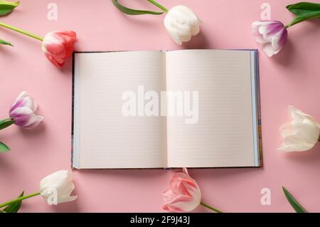taccuino vuoto su sfondo rosa con cornice di bellissimi fiori. Mockup floreale. Concetto di planatrice. Spazio per testo. Disposizione piatta, vista dall'alto Foto Stock