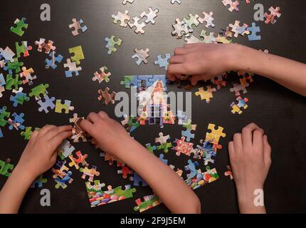 le mani dei bambini raccolgono il puzzle sul tavolo scuro. puzzle di gioco educativo. vista dall'alto. fuoco selettivo. Foto Stock