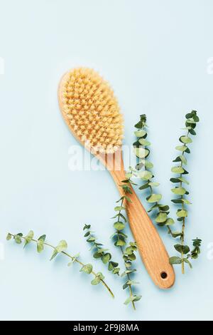 Concetto di trattamento SPA. Spazzola per massaggio anticellulite secco e rami di eucalipto su fondo blu. Vista dall'alto, spazio di copia per il testo Foto Stock