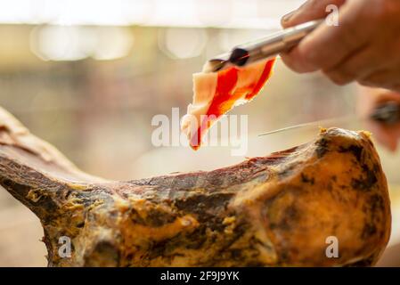 Primo piano sulle mani della persona affettando deliziosa scultura di prosciutto cured Foto Stock