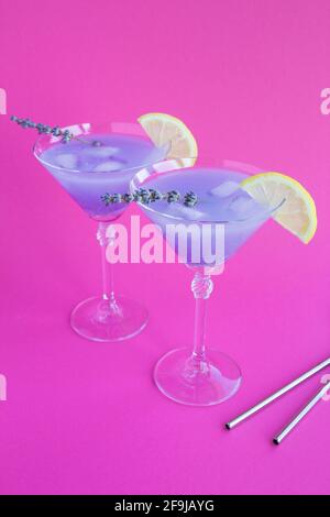 Limonata di lavanda con limone e ghiaccio in bicchieri martini su sfondo rosa brillante. Posizione verticale. Foto Stock