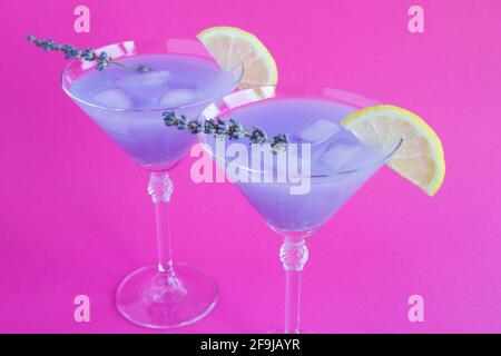 Limonata di lavanda con limone e ghiaccio in bicchieri martini su sfondo rosa brillante. Primo piano. Foto Stock