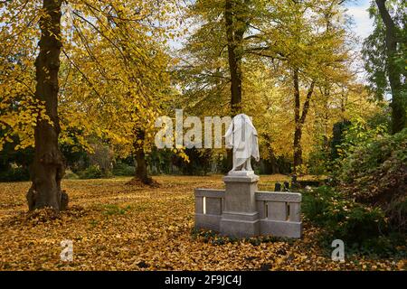 Grabmal mit beschädigter statue einer Frau, Frau ohne Kopf, Bäume im Herbstlaub, Luisenstädtischer Friedhof, Kreuzberg, Berlino, Germania Foto Stock