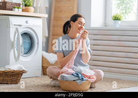 Bella giovane donna sta sorridendo mentre facendo lavanderia a casa. Foto Stock