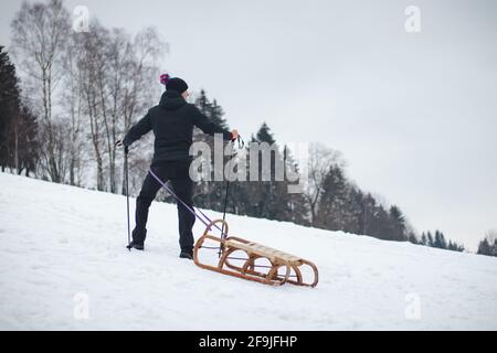 un giovane uomo che indossa una giacca blu e un cappuccio bianco corre lungo la collina utilizzando bastoncini da trekking per una maggiore stabilità e una discesa migliore senza cadute. Inverno montagna RU Foto Stock