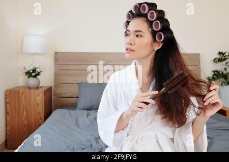 Ritratto di sorridente giovane donna asiatica che sfrega i capelli e si applica rulli per capelli Foto Stock