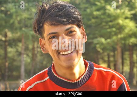 Primo piano di un giovane ragazzo indiano sorridente all'aperto con una fotocamera, Laughing giovane ragazzo - Stock Photo Foto Stock