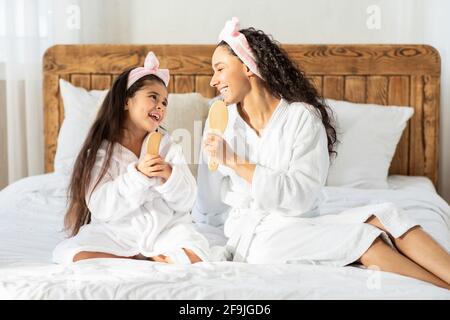 Mamma e figlia divertenti con spazzole per capelli che cantano a casa Foto Stock