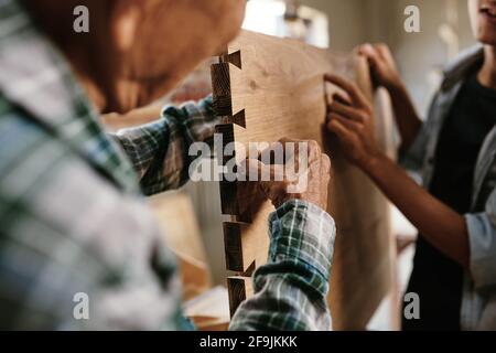 Immagine ravvicinata del carpentiere esperto senior che controlla il taglio e la levigatura tavola di legno fatta per il cliente Foto Stock