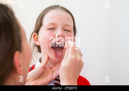 Età scolastica bambino scuola primaria ragazza di nove anni / 9 anni che ha campioni prelevati dalla gola per l'uso in un LFT di test di flusso laterale dalla società cinese Innova. Inghilterra Regno Unito. (123) Foto Stock