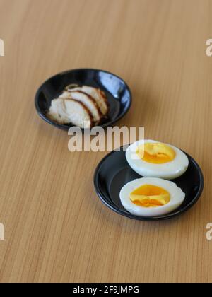 Ingredienti ricette giapponesi. Pollo affettato e uovo bollito su piatto nero Foto Stock