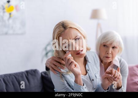 Piangendo la donna con il tovagliolo seduto vicino al genitore anziano su offuscato sfondo Foto Stock