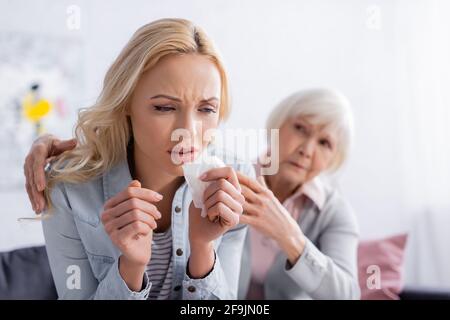 Donna dispiaciuta seduta vicino madre anziana su sfondo sfocato Foto Stock