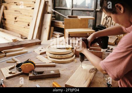 Giovane donna che perfora i fori in legno su banco da lavoro Foto Stock