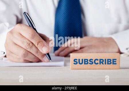 La parola subscribe scritta su un blocco di legno di fronte ad un uomo d'affari che riempie un modulo sullo sfondo. Abbonamento, registrazione e abbonamento con Foto Stock