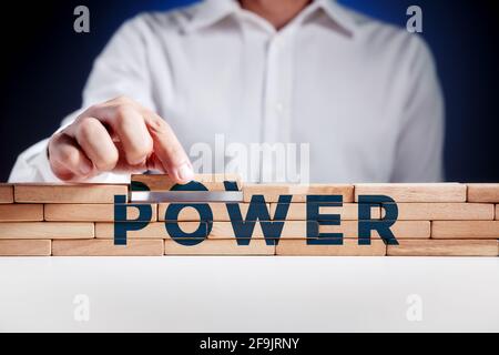 L'uomo costruisce una struttura di blocchi di legno con la parola potere. Costruire il potere nel concetto di economia o politica. Foto Stock