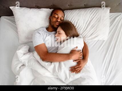 Vista dall'alto della coppia multirazziale affettuosa che si agganava l'un l'altro mentre dormire nel letto Foto Stock
